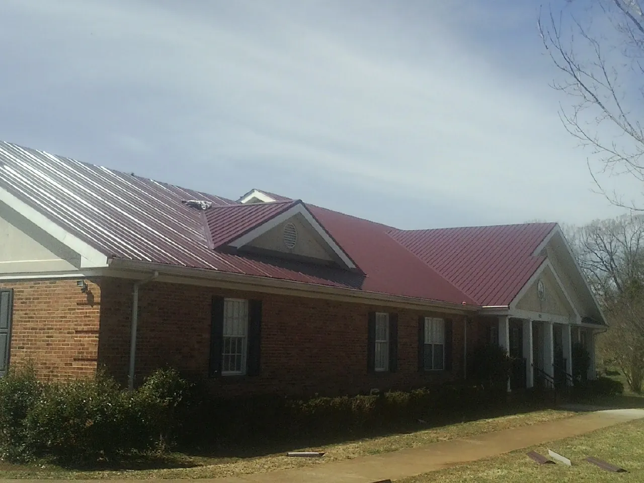 Red metal roof with gabled entries on a long brick building, from a Hail Damage Roof Repair job in Santo Domingo Pueblo