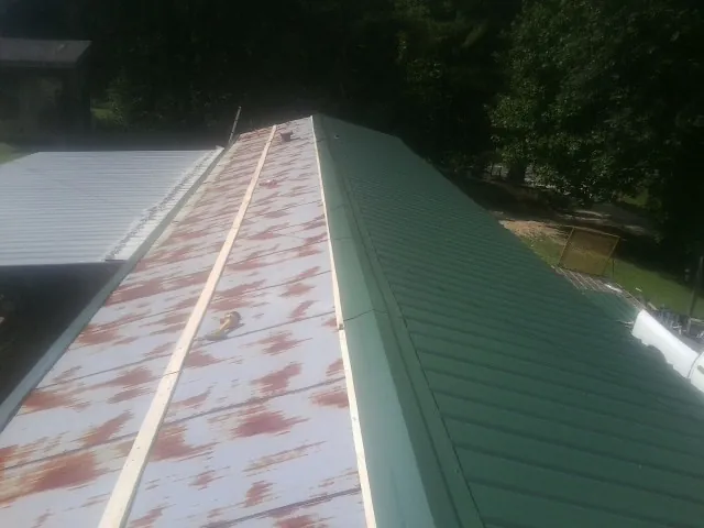 Old rusted panels beside newly installed green metal roofing — Wind Damage Roof Repair by Roofing Brothers in Santo Domingo Pueblo