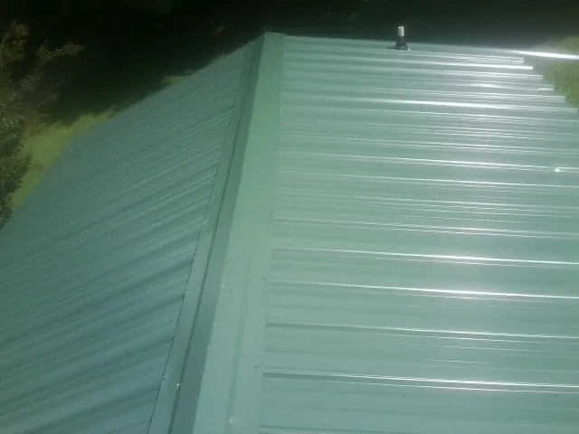 New green metal panels meeting at the ridge of a roof — Flat Roof Repair work by our crew in Santo Domingo Pueblo