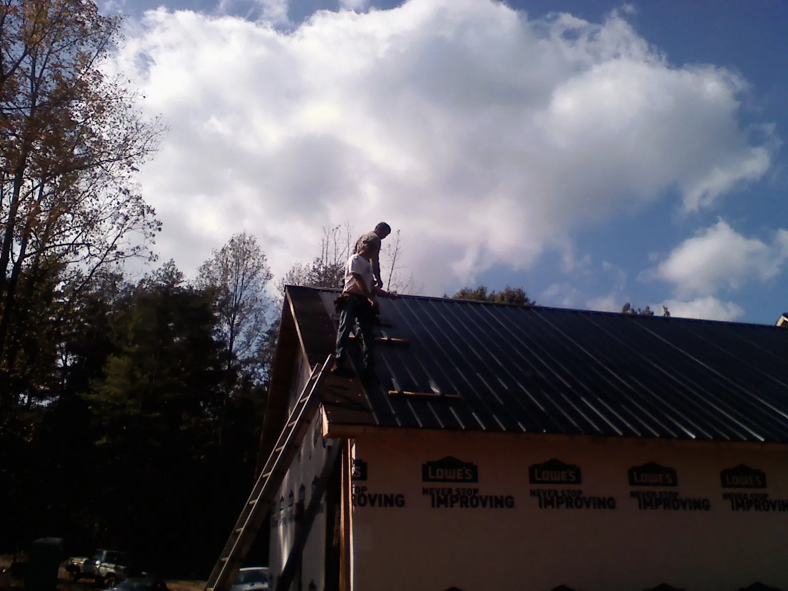 Roofer fastening dark metal panels high against a cloudy sky, from a Roof Inspection job in Santo Domingo Pueblo