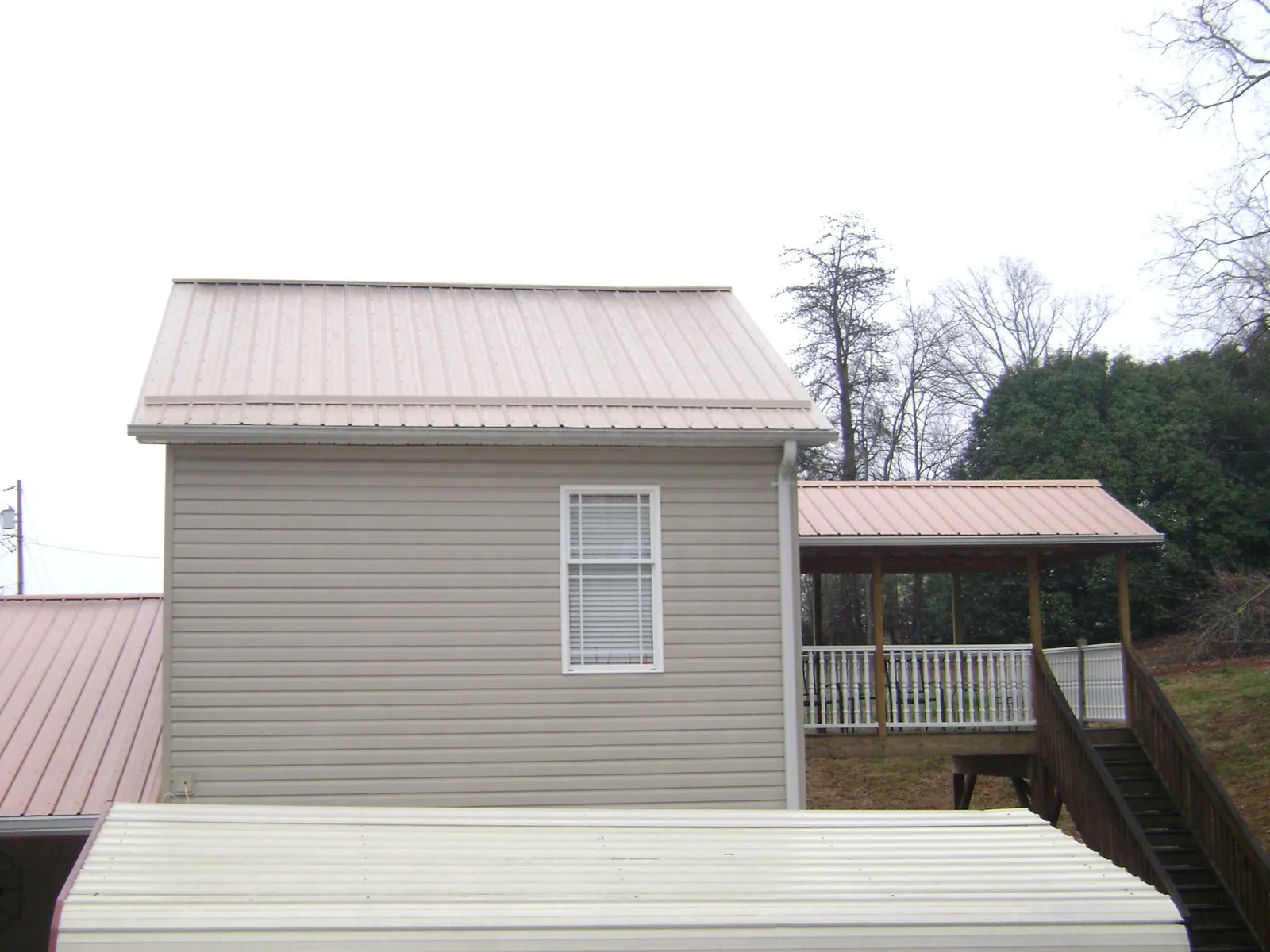 Tan metal roofs on a two story addition and attached porch, from a Roof Replacement job in Santo Domingo Pueblo